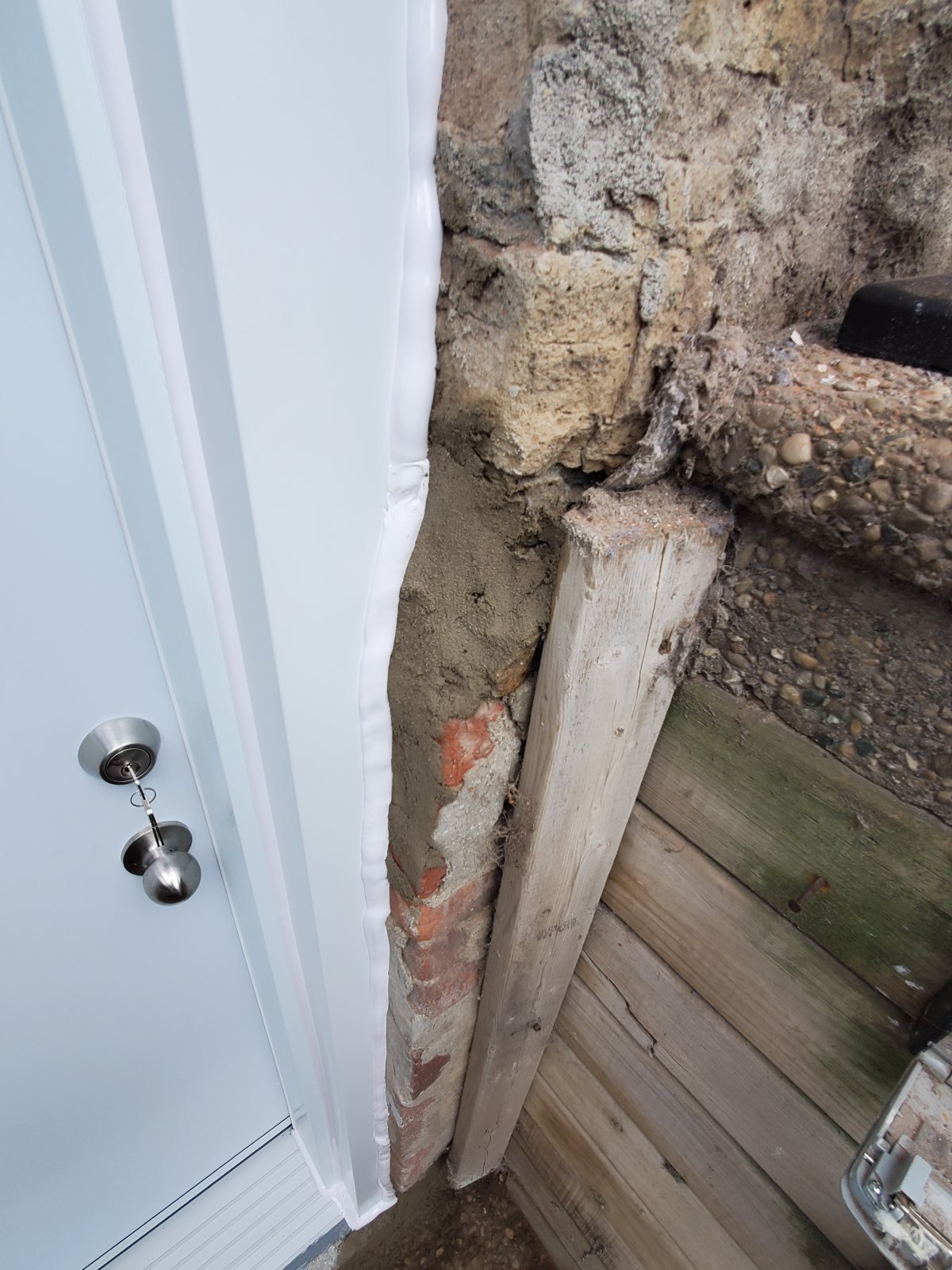 Close detail of a white exterior door jamb beside older masonry