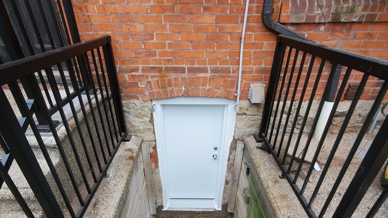 White exterior door at the bottom of a brick and concrete stairwell